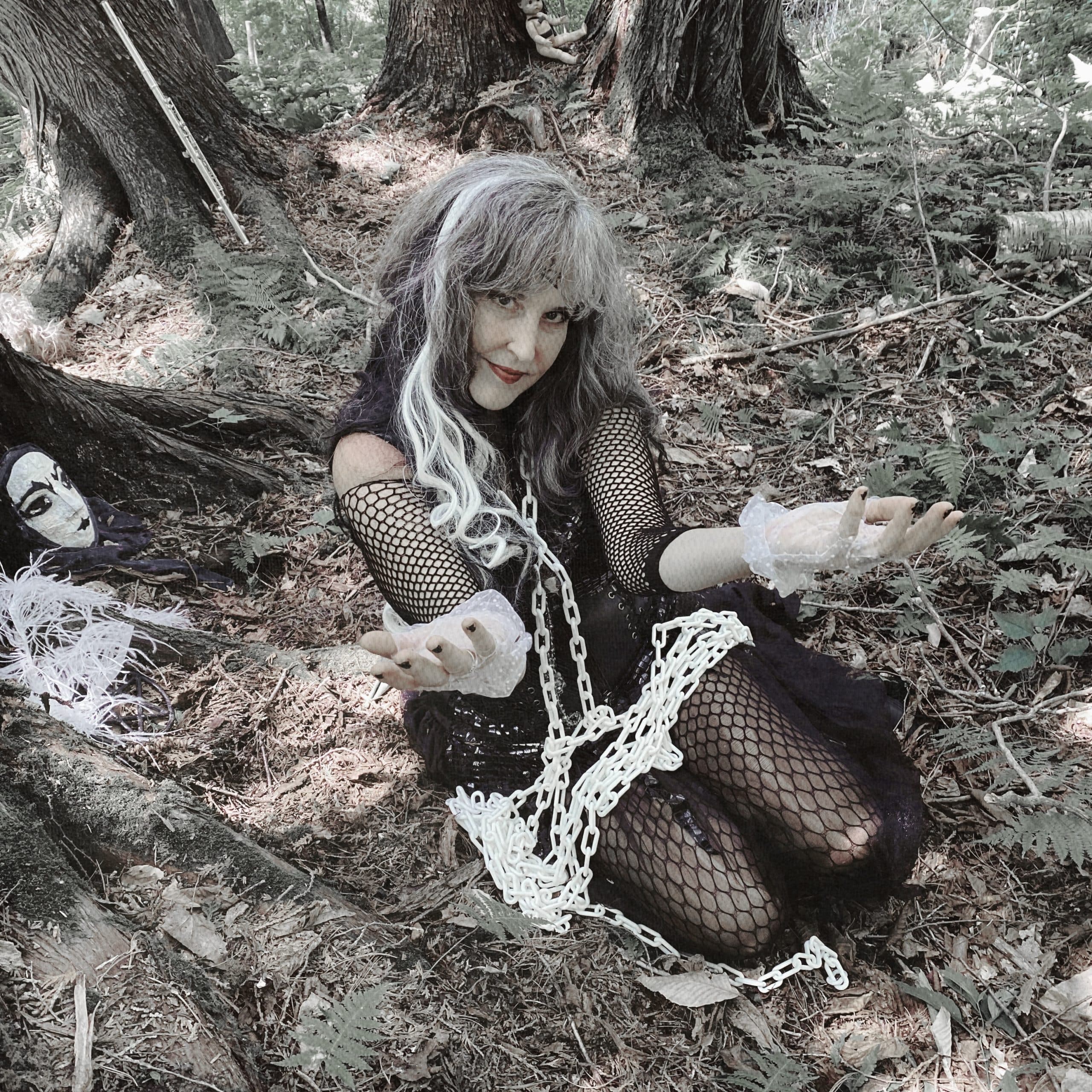 A woman in a costume sitting on the ground in a wooded area.