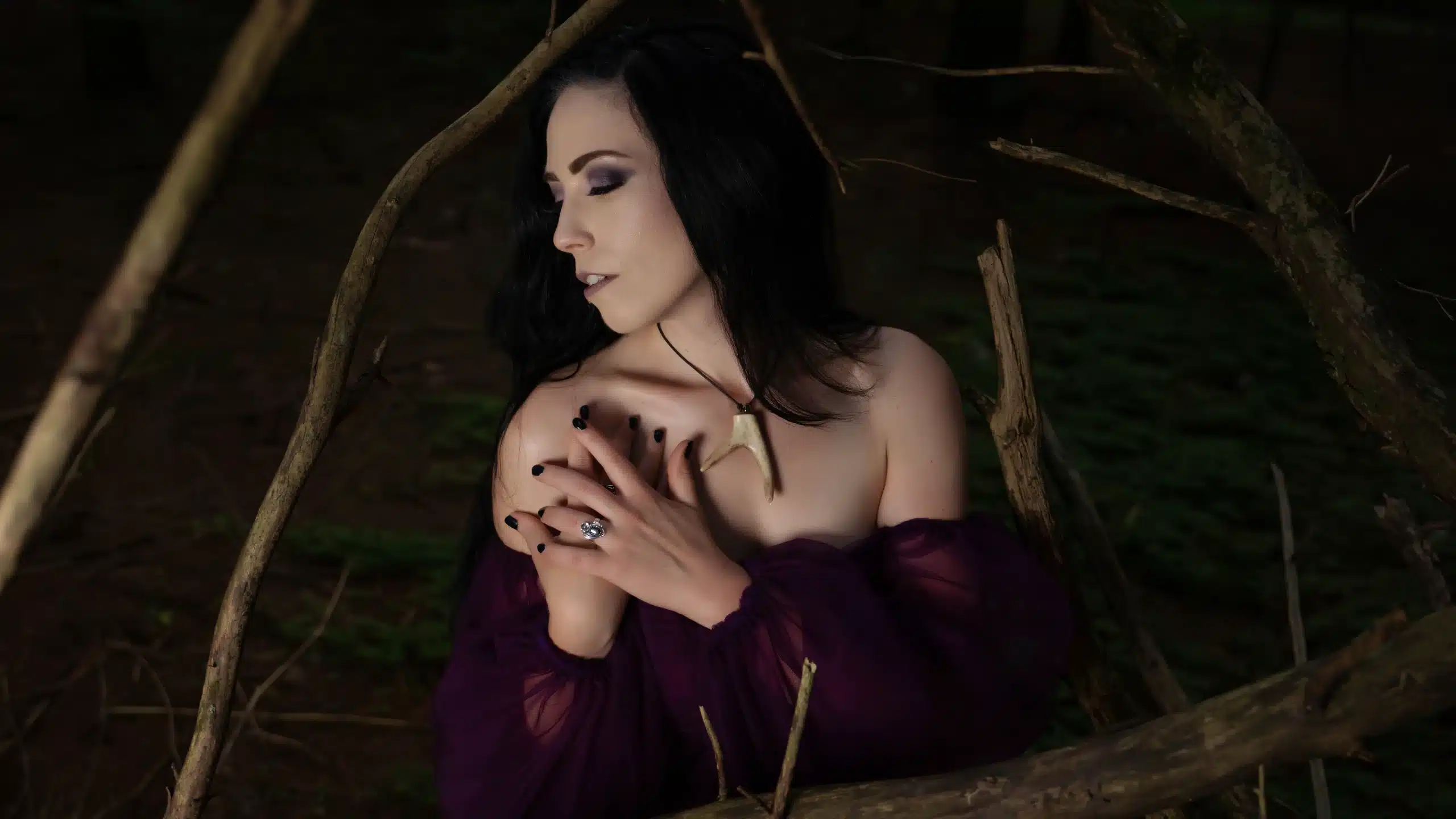 A woman in a purple dress is posing in the woods.