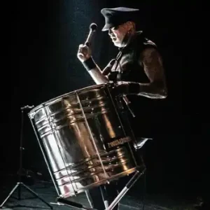 A man, filled with great sadness, plays a drum on stage.