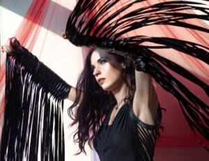 A woman with black feathers posing in front of a curtain.