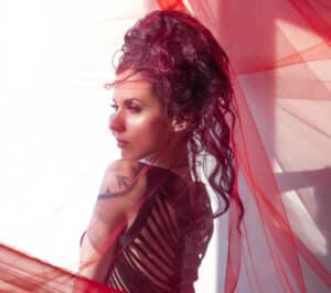 A woman in a red dress posing in front of a curtain.