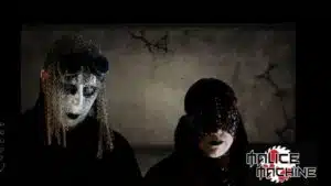 Two individuals wearing dark, gothic attire and masks with a sinister aesthetic.