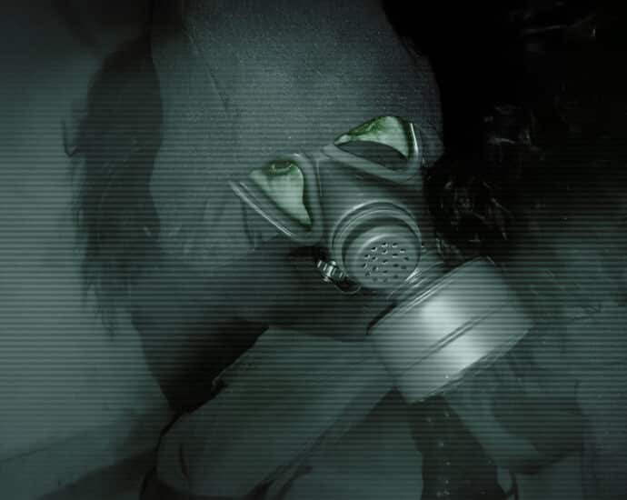 Person wearing a gas mask and hooded jacket, crouching in a dimly lit environment, viewed through grainy, green-tinted night vision.