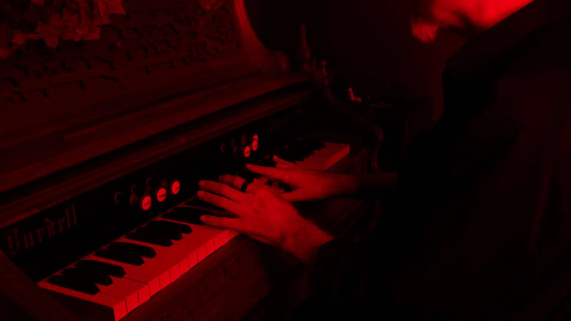 A person plays a vintage keyboard under red light, echoing the haunting melody of a Funeral March.