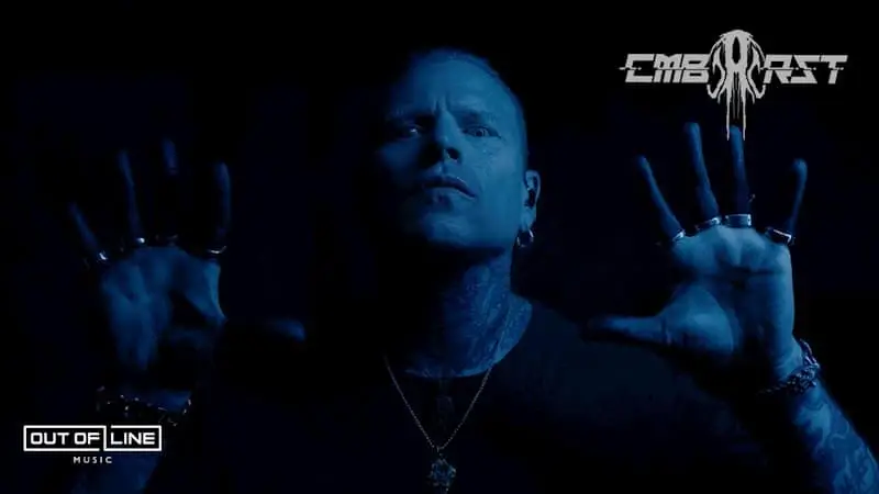 A person with tattoos and rings holds their hands up in front of them. The image has a blue tint. "Out of Line Music" and "Combichrist" logos appear in the corners.